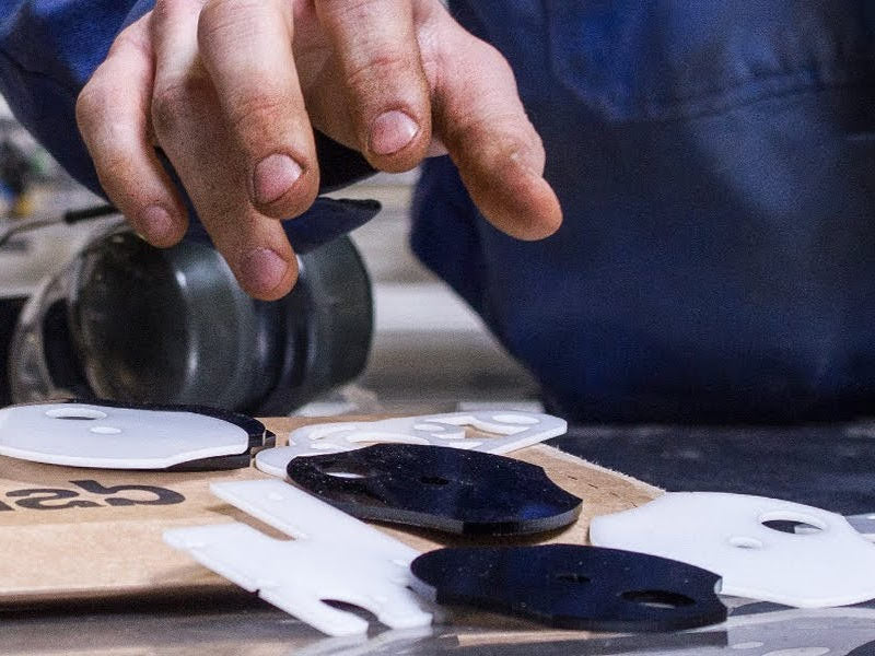 close up of someone picking up plastic laser cut technical parts from a workbench. An envelope with a snijlab logo is visible next to the parts.